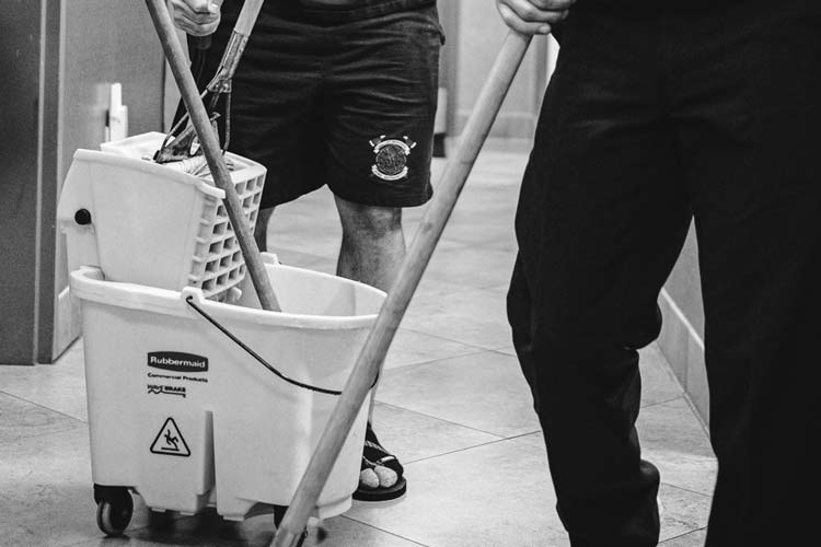 Two firefighters standing next to a mop and bucket.