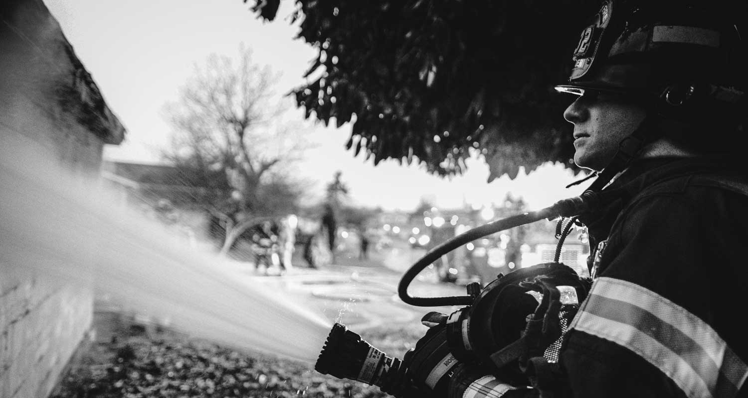 Firefighter spraying hose at house fire