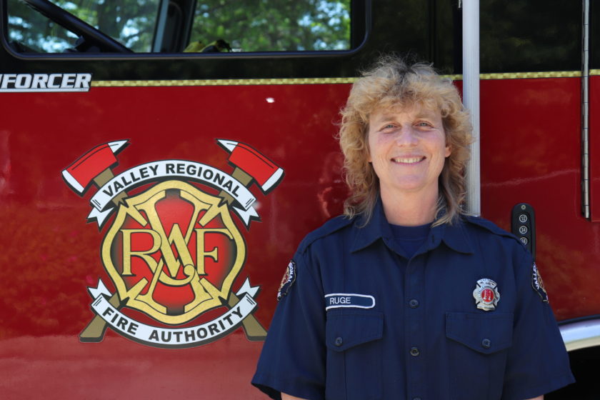 A firefighter in uniform standing in front of a fire truck.