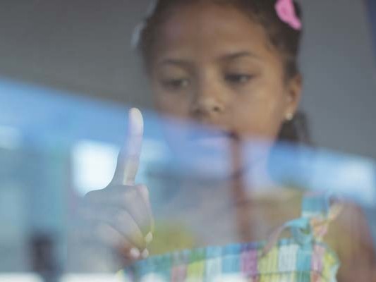 Girl touching glass window with index finger