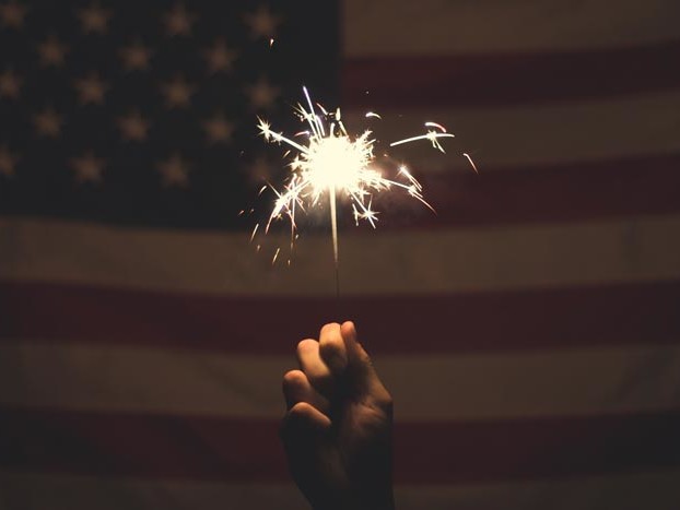 Hand holding sparkler with American flag in the background
