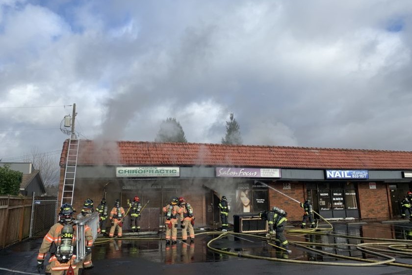 A firefighter from the Fire Department is bravely battling a fire in front of a building, providing essential service and risking their life to ensure the safety and rescue of those inside.