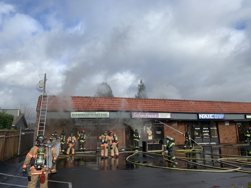 A firefighter from the Fire Department is bravely battling a fire in front of a building, providing essential service and risking their life to ensure the safety and rescue of those inside.