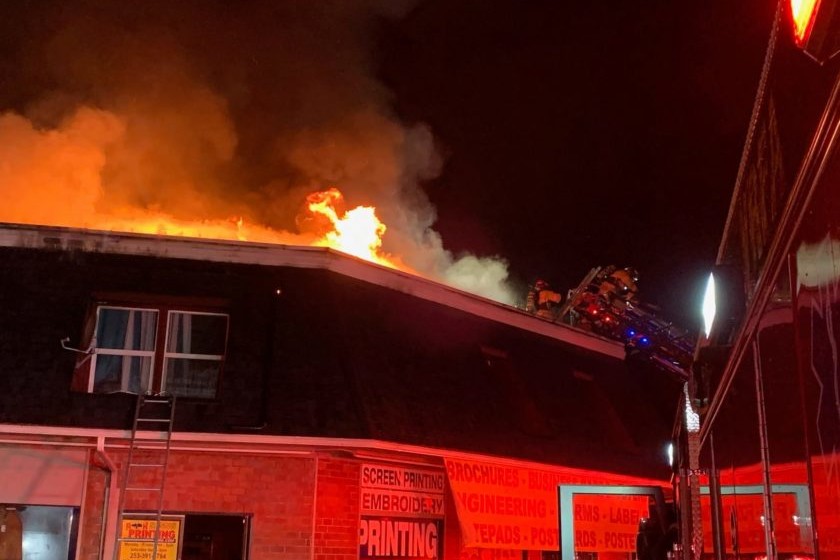 A firefighter rescuing people from a fire on the roof of a building at night.