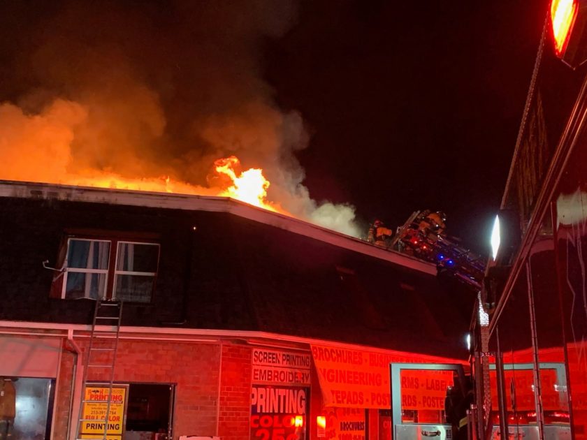 A firefighter rescuing people from a fire on the roof of a building at night.