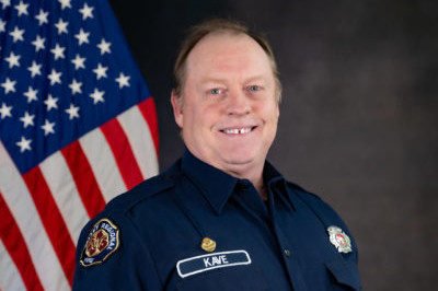 A firefighter in uniform standing in front of an american flag.