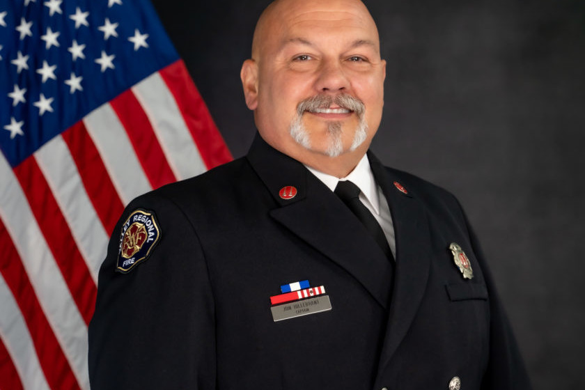 A man in a firefighter uniform standing in front of an american flag, representing the dedication and service of the Fire Department.