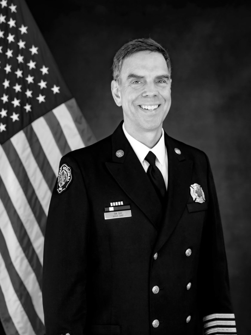 A black and white photo of a firefighter standing in front of an American flag, embodying service and dedication.