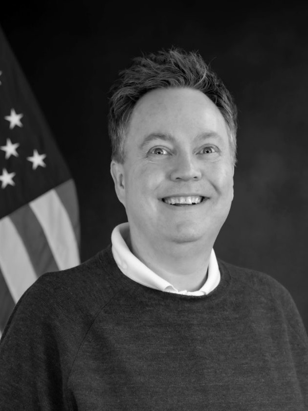 A black and white photo of a firefighter smiling in front of an American flag.