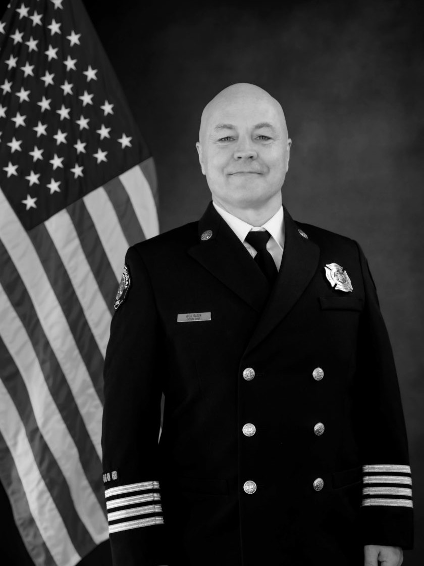 A black and white photo of a firefighter from the Valley Regional Fire Authority standing in front of an American flag.