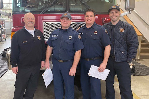 Four firefighters from the Fire Department standing in front of a fire truck, ready for service and rescue.