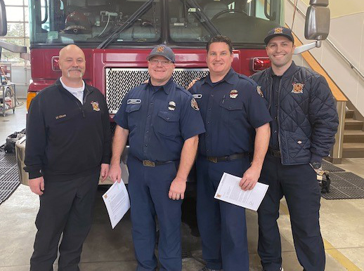 Four firefighters from the Fire Department standing in front of a fire truck, ready for service and rescue.