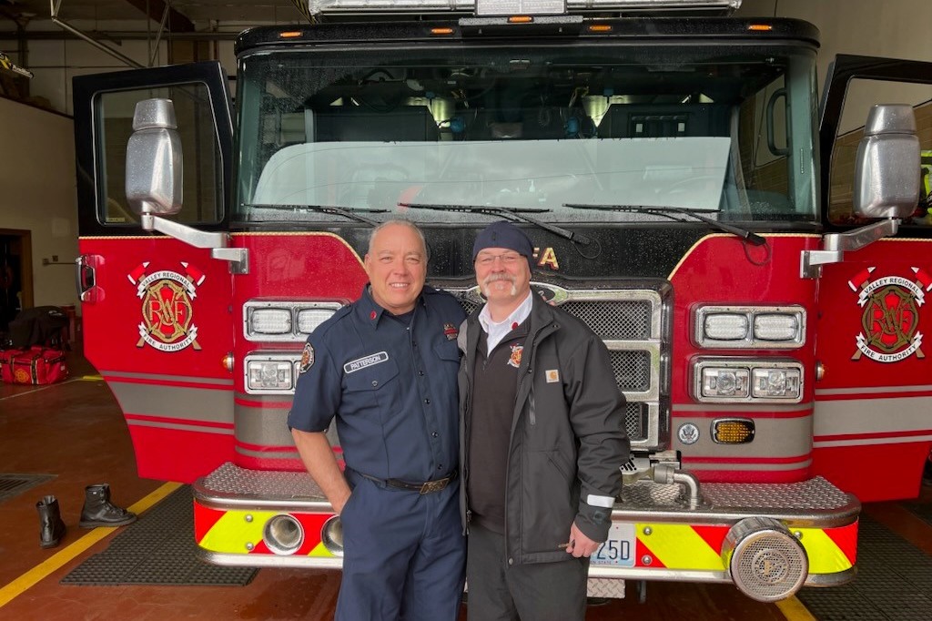 Two men from the fire department standing in front of a fire truck.