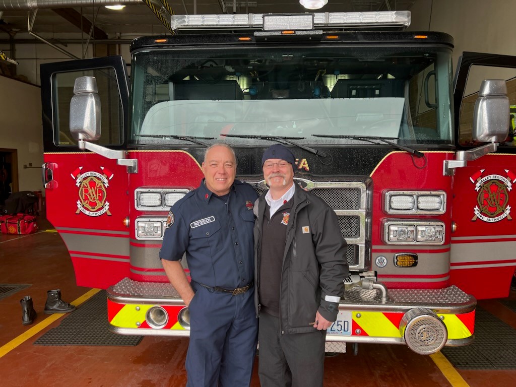 Two men from the fire department standing in front of a fire truck.