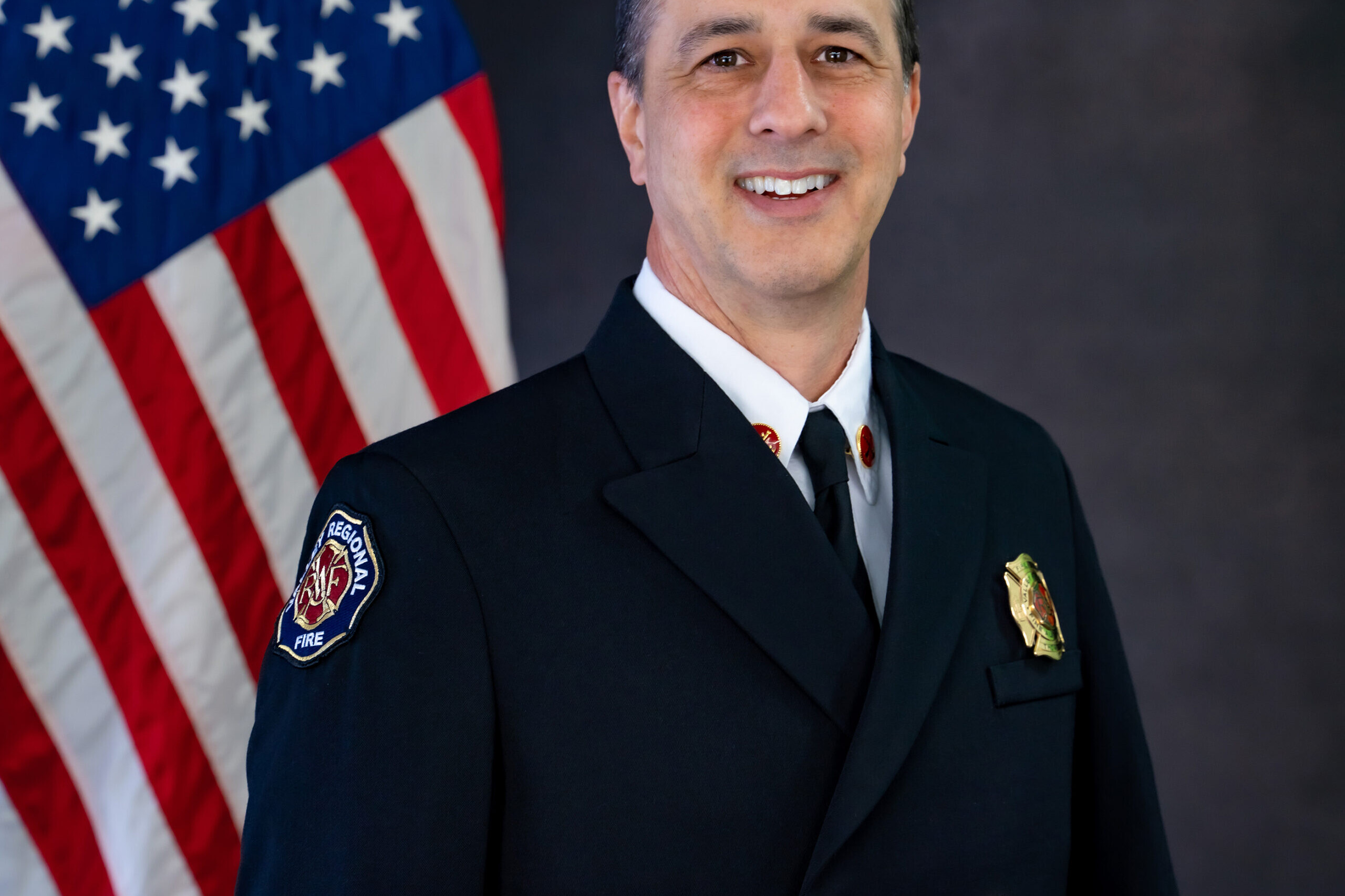 A man in a Fire Department uniform standing in front of an American flag.