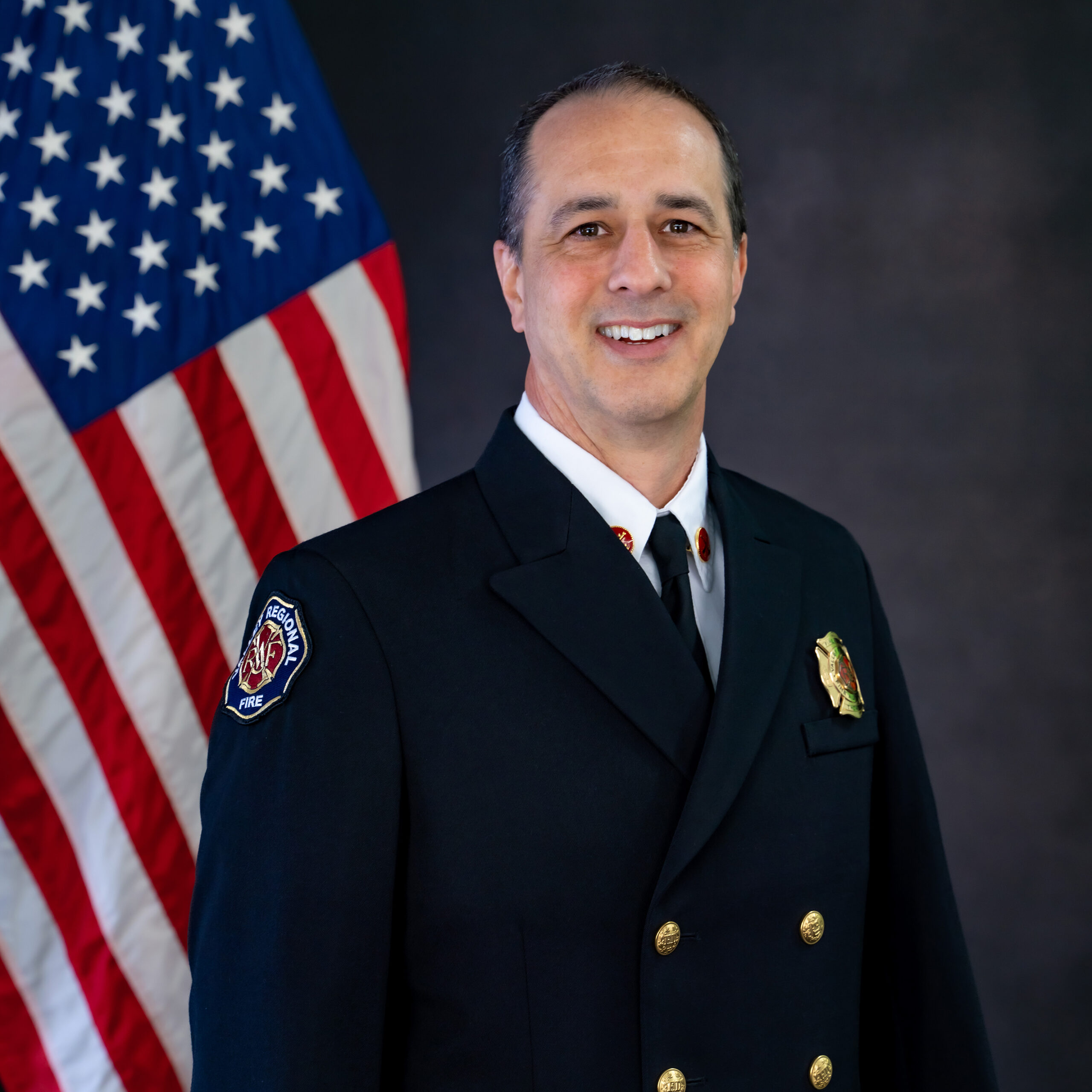 A man in a Fire Department uniform standing in front of an American flag.
