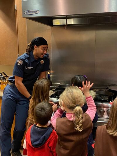 A boy scout cooking with kids in a kitchen, providing a service to teach them valuable cooking skills.