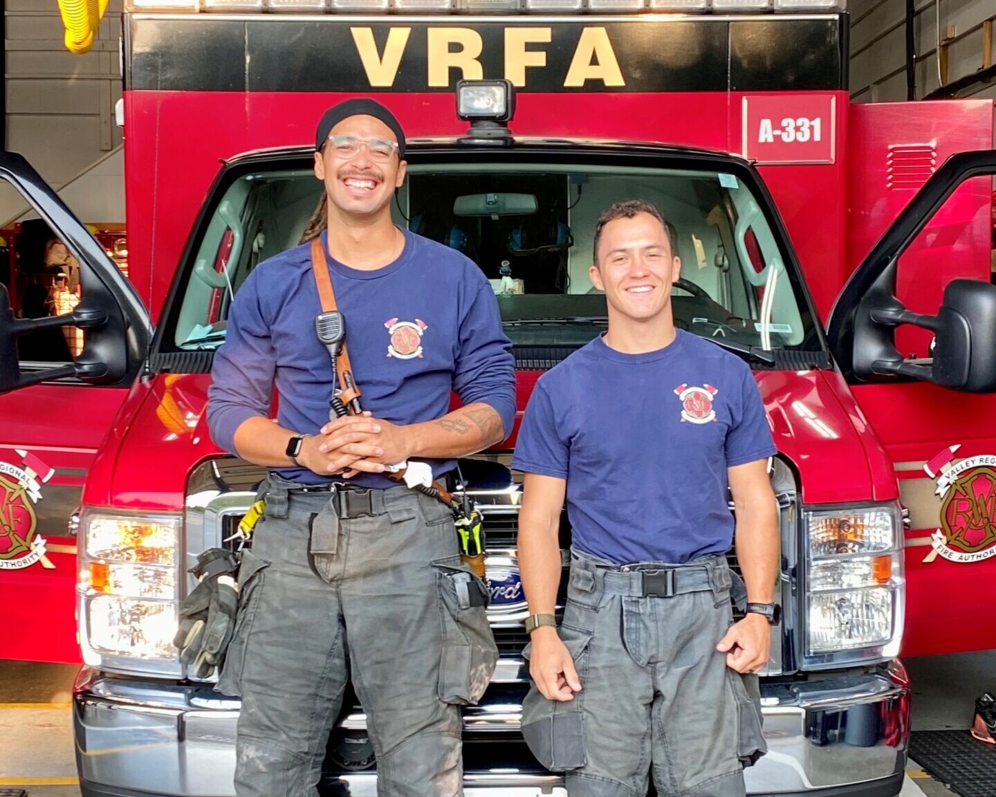 Two firefighters smiling in front of fire engine