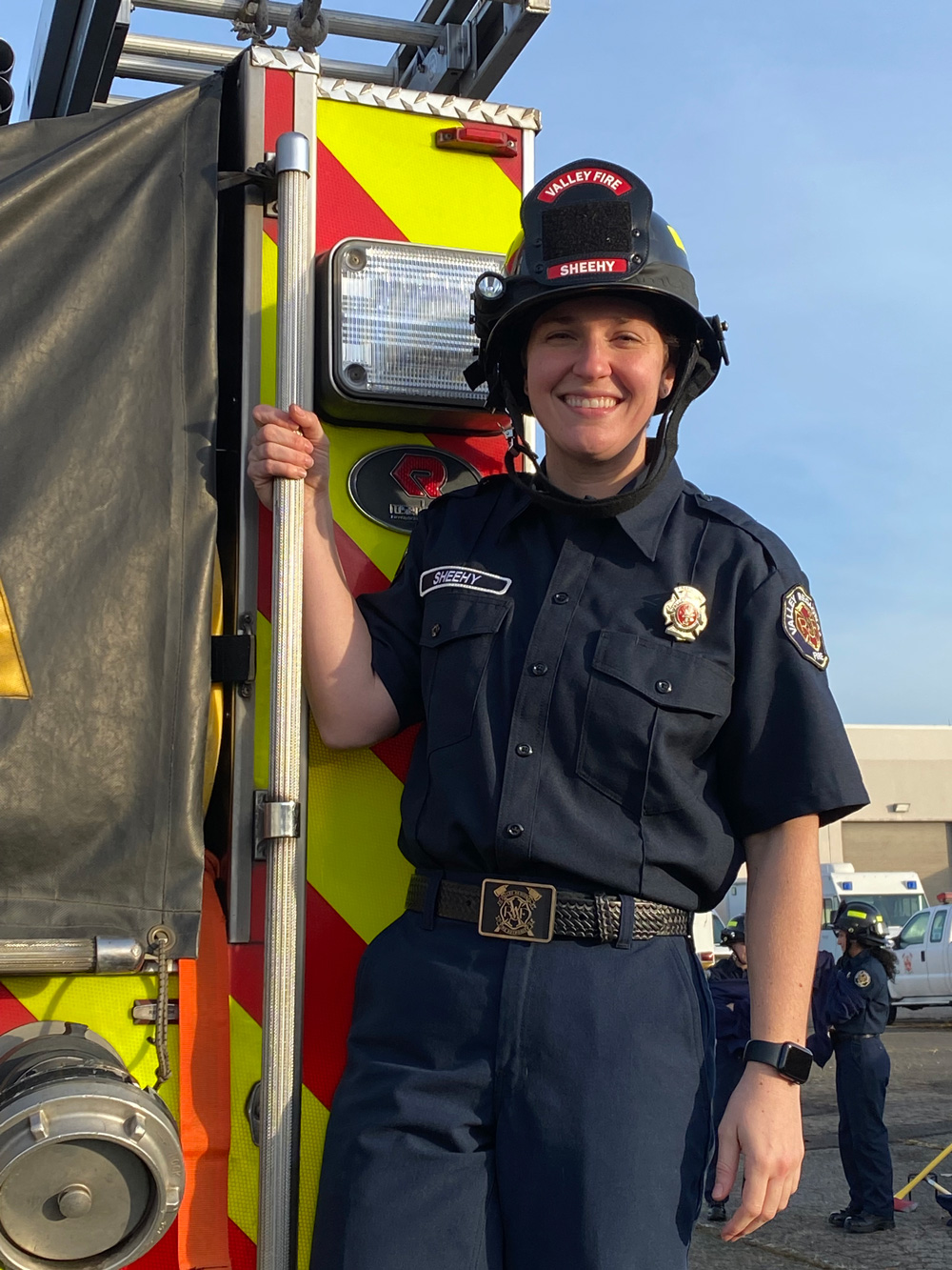 Female firefighter holding onto back of fire engine