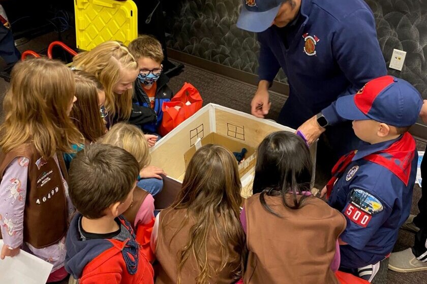 A boy scout discusses fire safety with a group of children in a classroom.