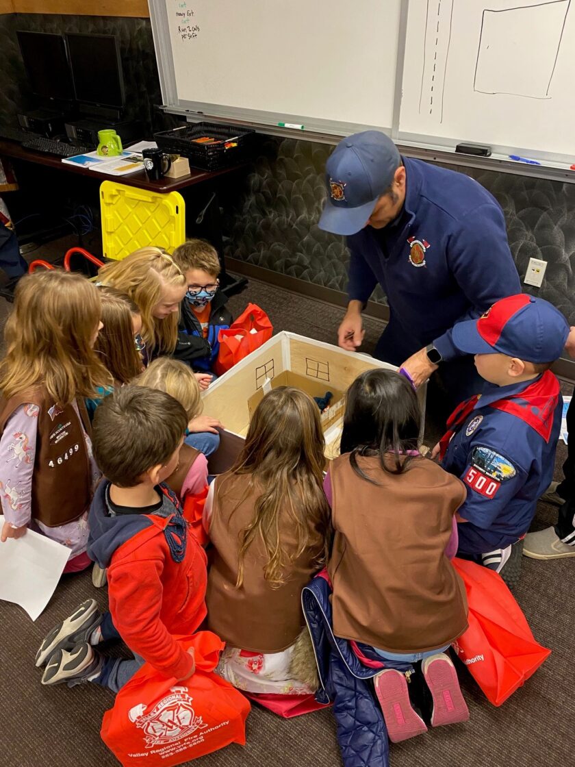 A boy scout discusses fire safety with a group of children in a classroom.