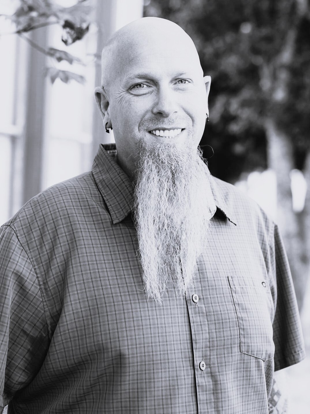 A black and white photo of a bald man with a beard, portraying confidence and authority.