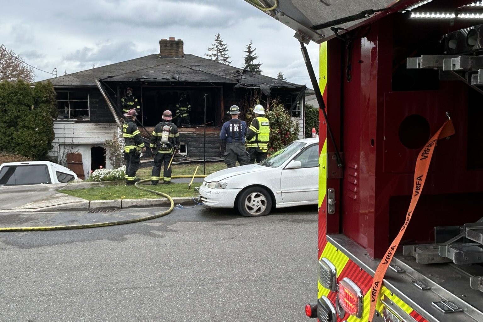 Firefighters rescue one person from a residential fire as seen from the open back of a fire truck.