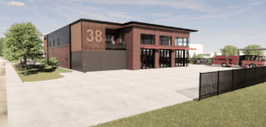 Modern two-story brick fire station with large garage doors, labeled "38," and a fire truck parked under a canopy on the right. Trees and grass border the paved area, showcasing progress from design to construction in our Capital Facilities Plan.