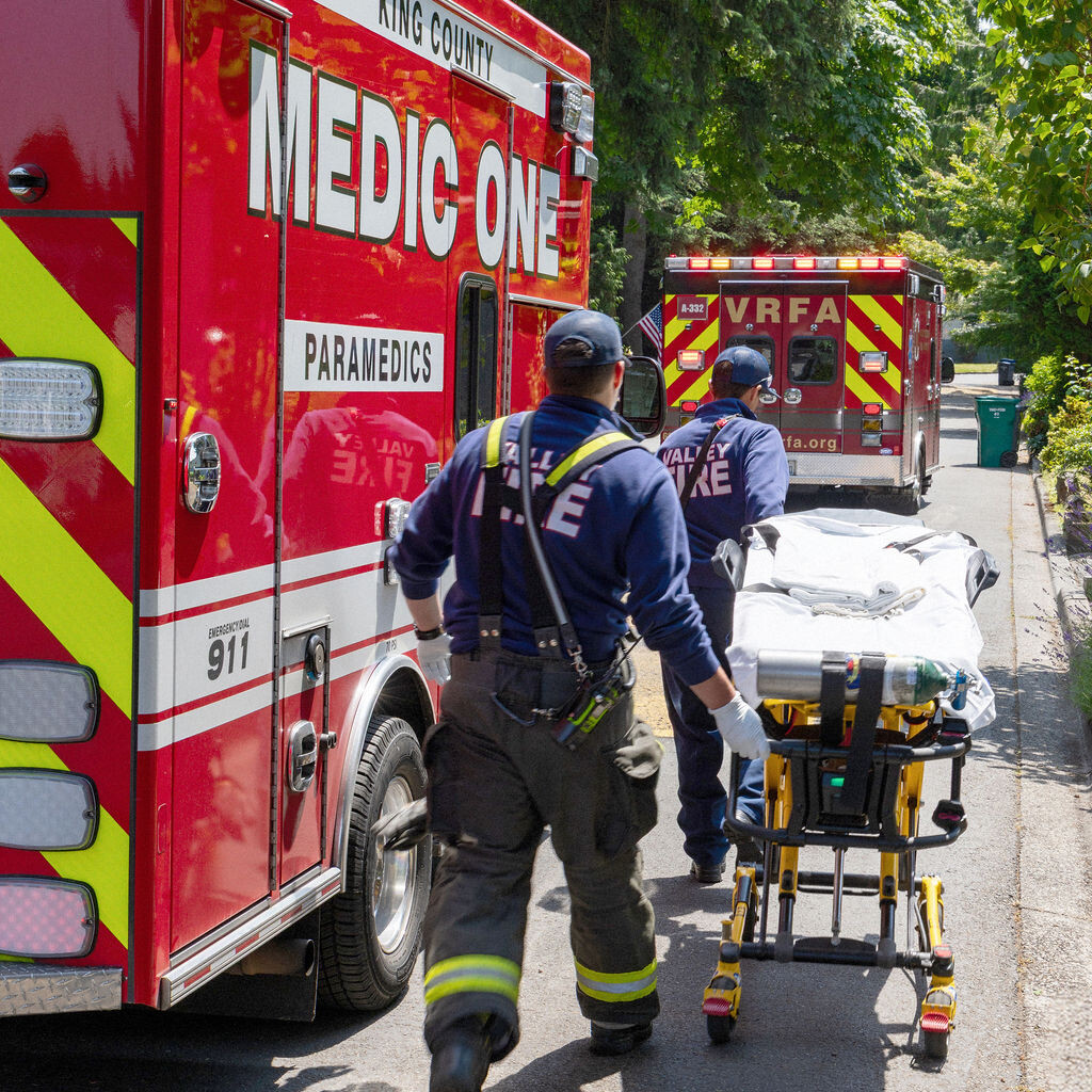 A paramedic pushes an empty stretcher toward an ambulance marked 
