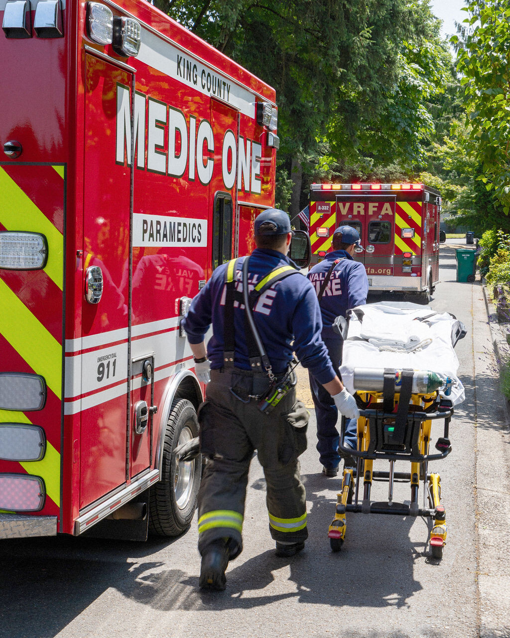 A paramedic pushes an empty stretcher toward an ambulance marked 