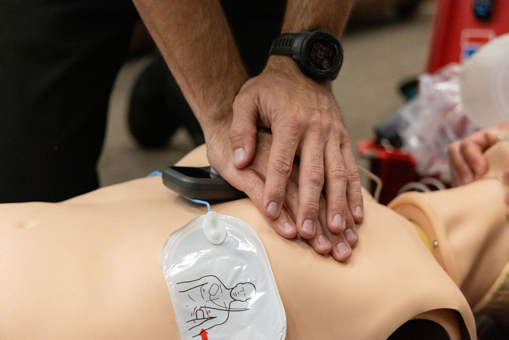 A person performs chest compressions on a CPR training manikin, with an automated external defibrillator (AED) pad attached to the manikin’s chest.