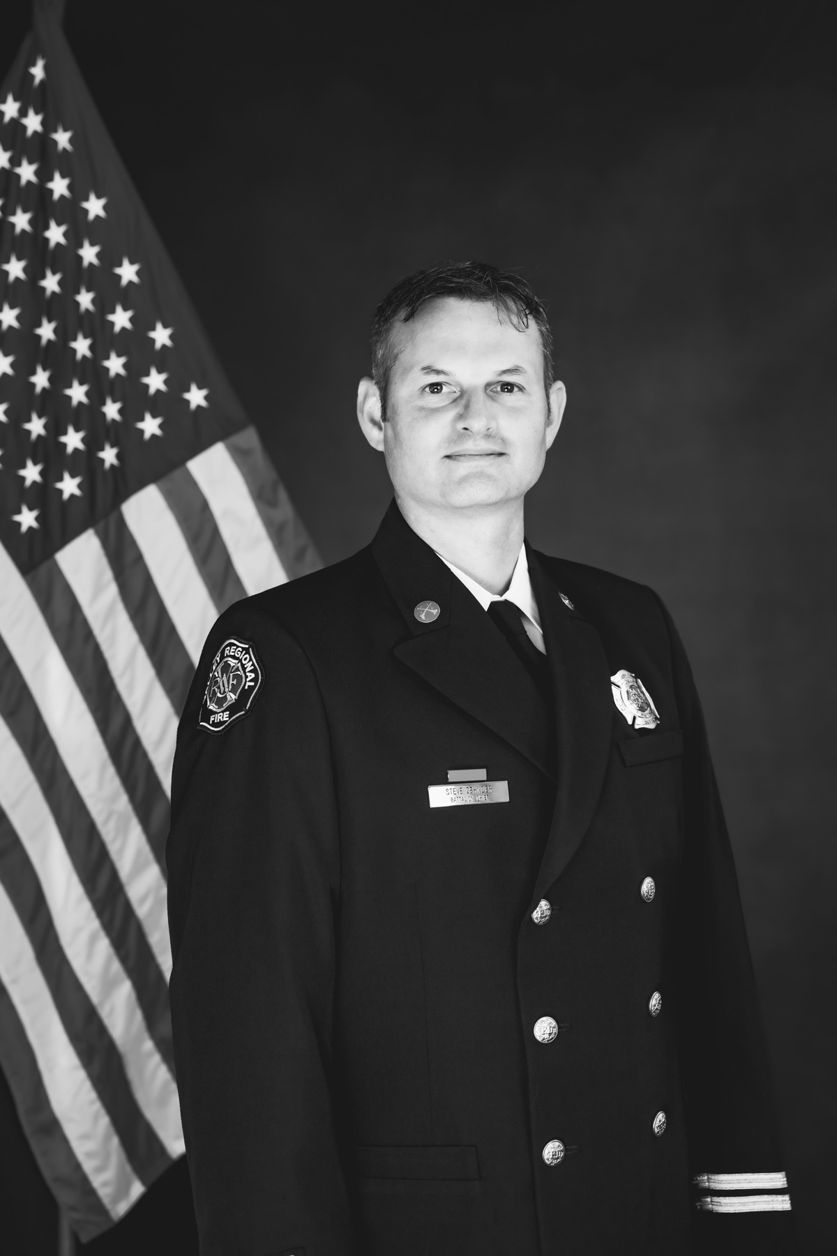 A firefighter in formal dress uniform stands in front of an American flag, representing dedication to public service and excellence in governance administration.