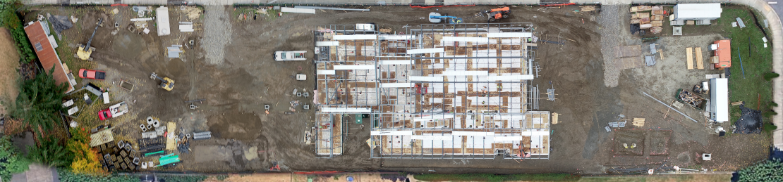 Aerial view of a construction site shows building progress on a partially built rectangular structure in the center, surrounded by heavy machinery, capital facilities, materials, and dirt.
