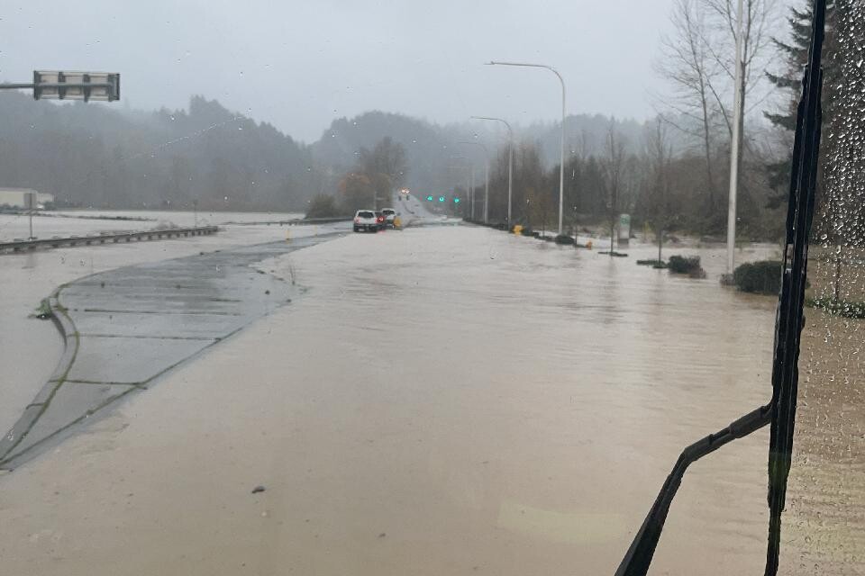 A flooded road with streetlights and vehicles partially submerged, viewed from inside an emergency response vehicle on a rainy day, highlights the urgent need for disaster assistance as local Disaster Assistance Centers open to support the affected community.