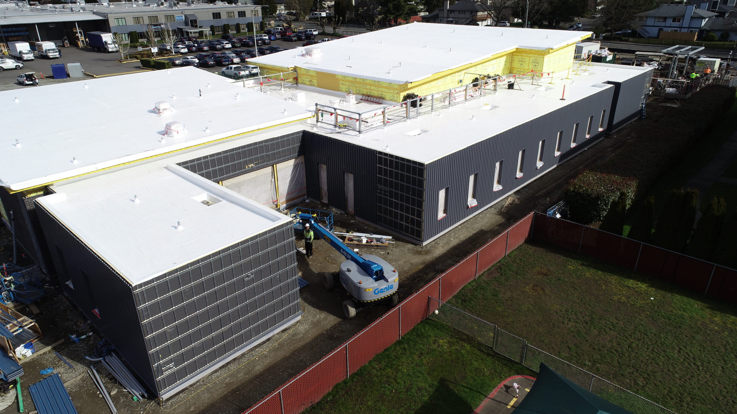 Aerial view of a modern building under construction, featuring white roofing, dark exterior walls, scaffolding, and a blue lift machine on site as part of the latest March 2026 Capital Projects update.