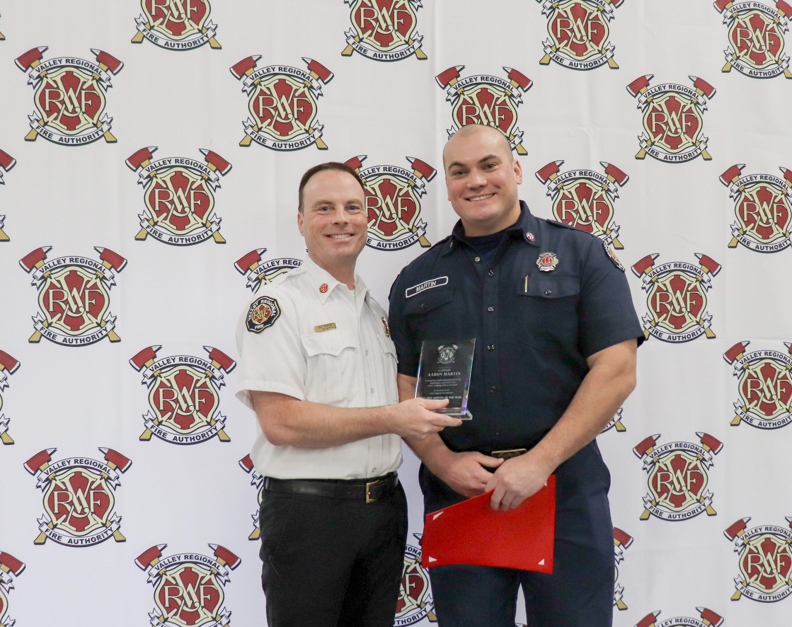 Two men in fire department uniforms stand together. Captain Aaron Martin is holding a plaque for Fire Officer of the Year, and both are smiling in front of a backdrop with the RMF and VRFA logos.