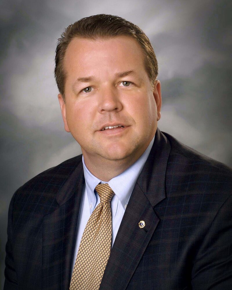 Eric Robertson, the founding administrator of Valley Regional Fire Authority, poses in a suit and tie for a formal portrait against a neutral, cloudy background.