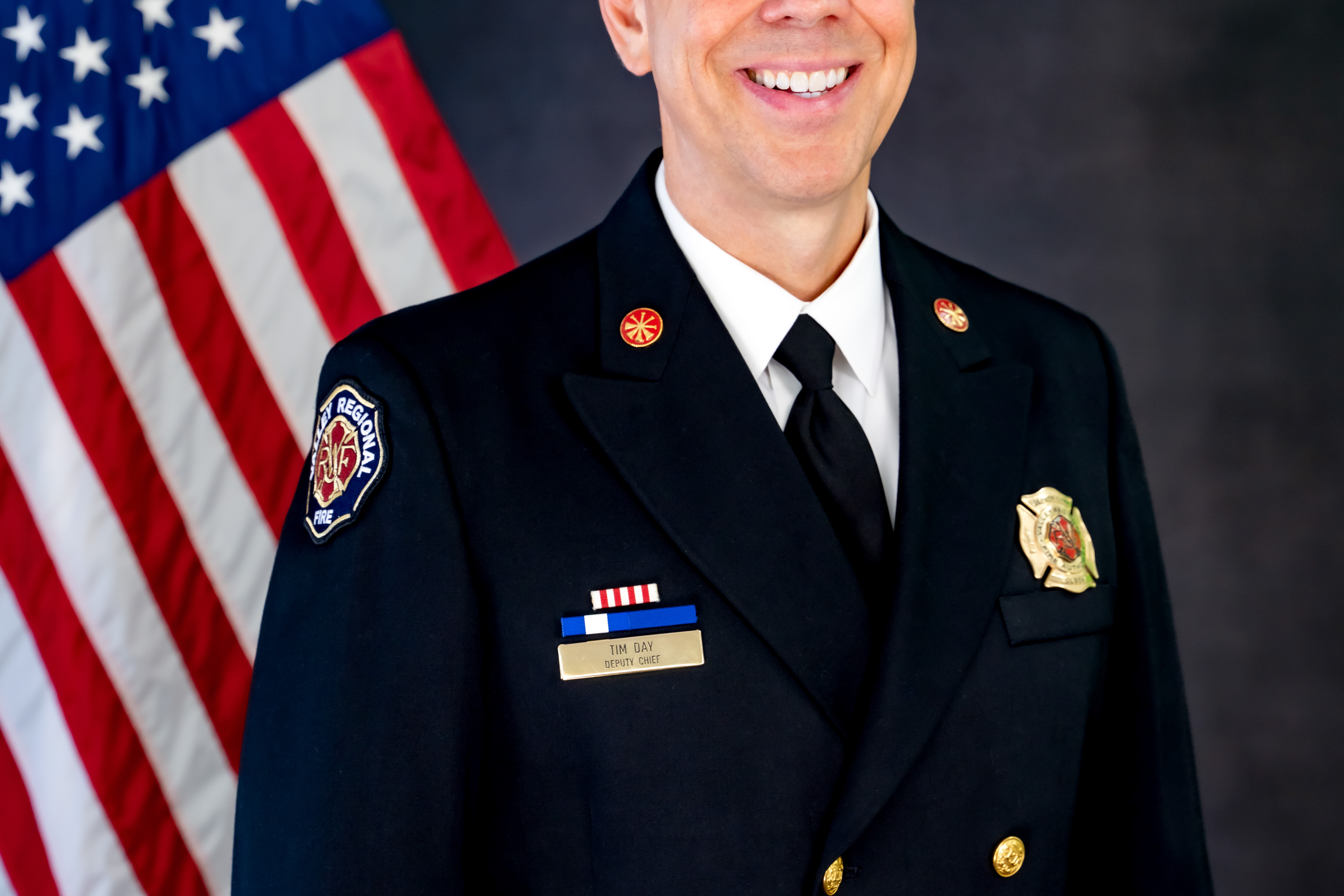 Fire Chief in Class A unifrom smiling in front of an american flag.