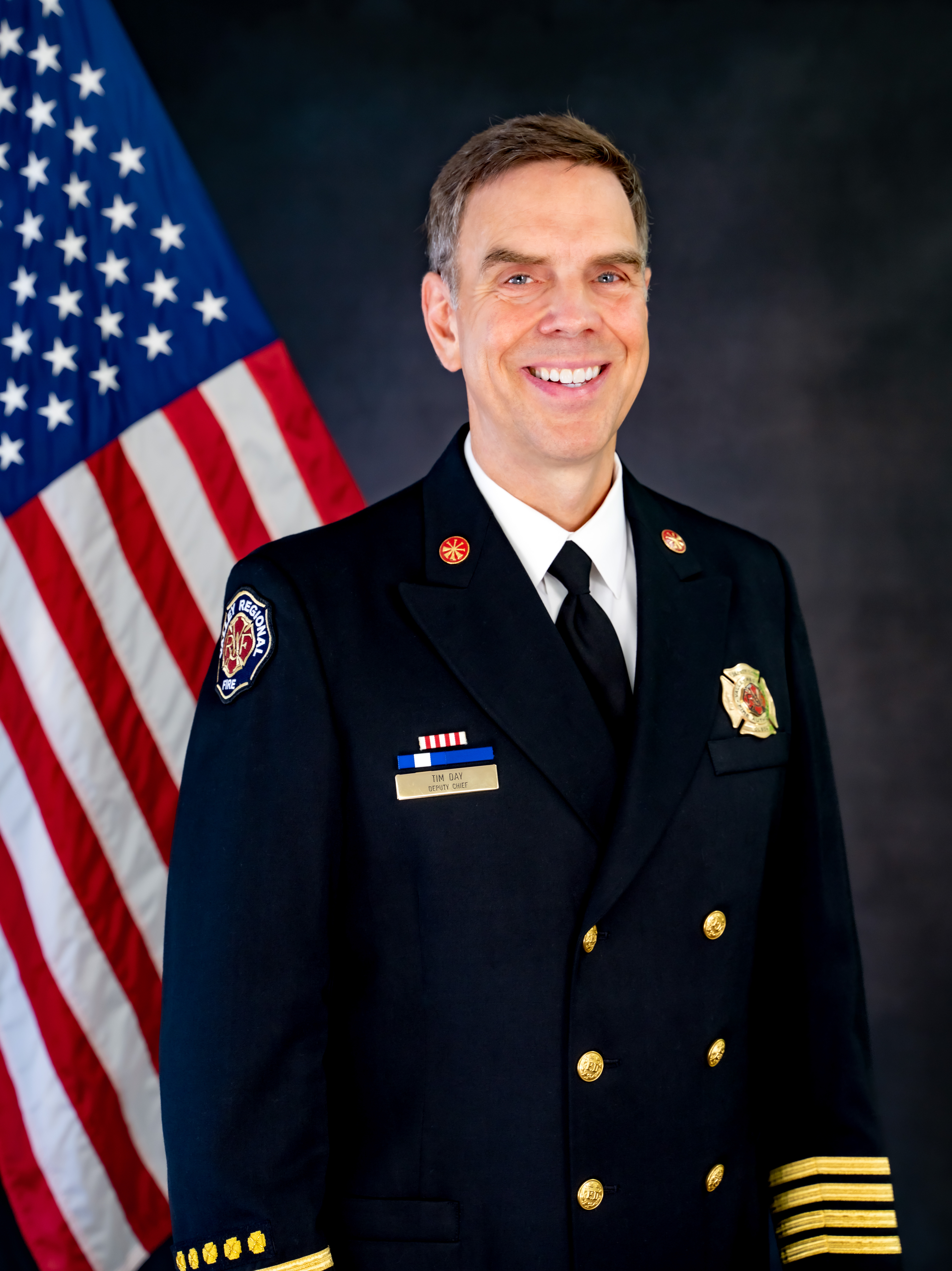 Fire Chief in Class A unifrom smiling in front of an american flag.